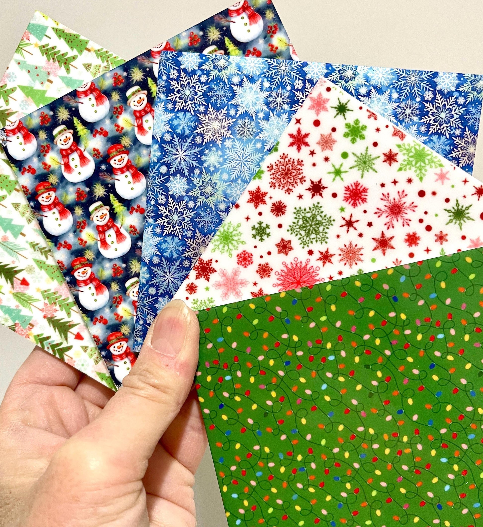 A hand holding a collection of colorful Christmas-themed paper cards.