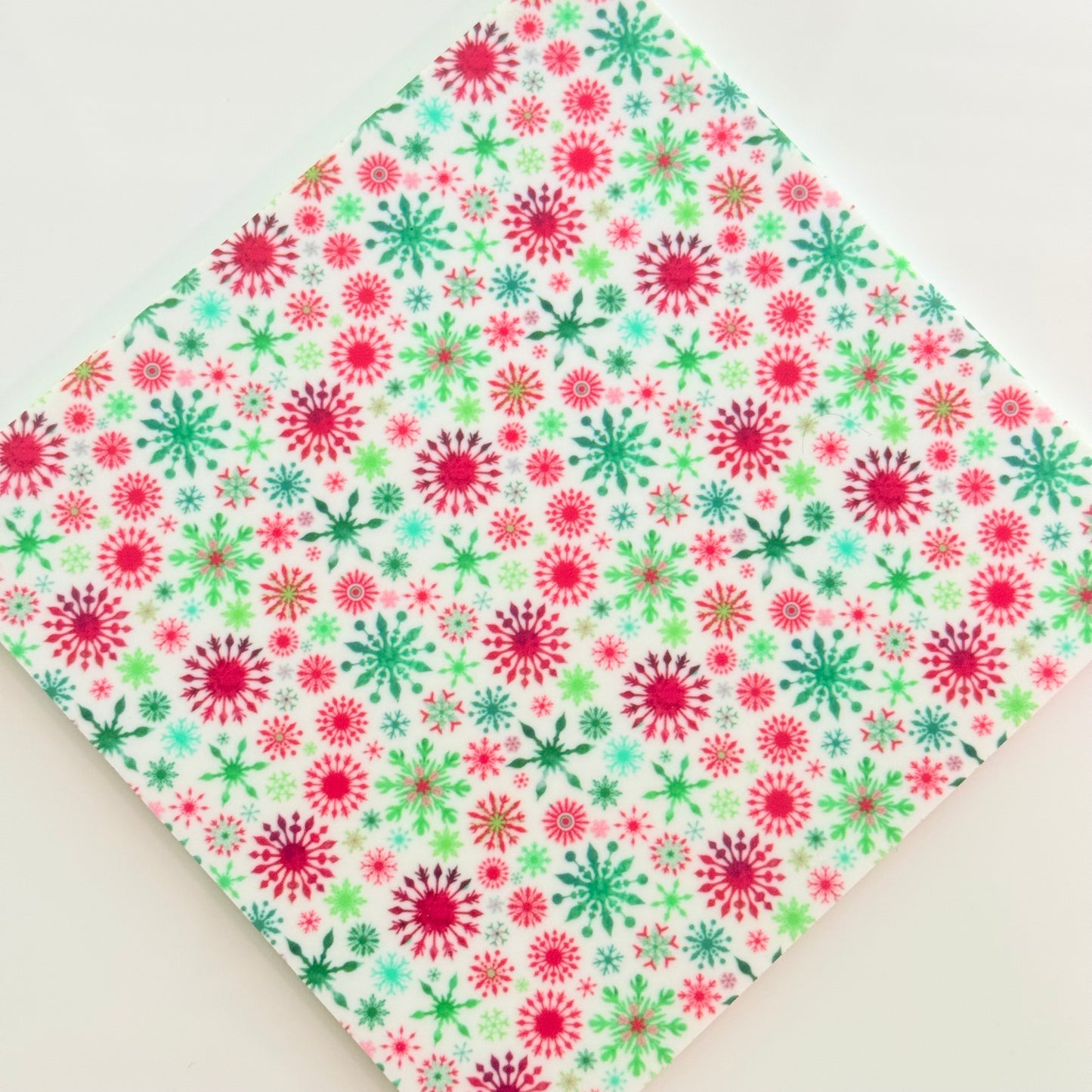 a white fabric with a vibrant, colorful pattern of red and green snowflakes.