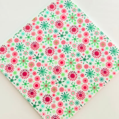 a white fabric with a vibrant, colorful pattern of red and green snowflakes.