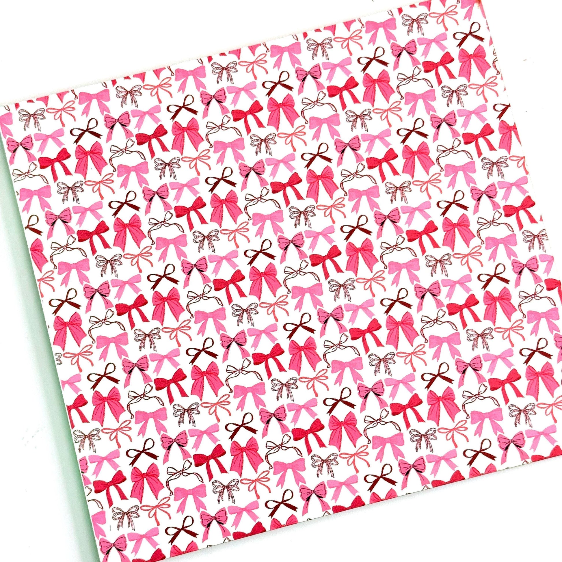 a repeating pattern of pink bows on a white acrylic background.