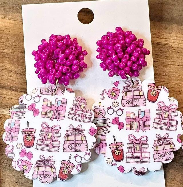 a pair of earrings with a pink bead design and a scalloped paper pattern featuring various pink and white illustrations, such as gift boxes, flowers, and other decorative elements.