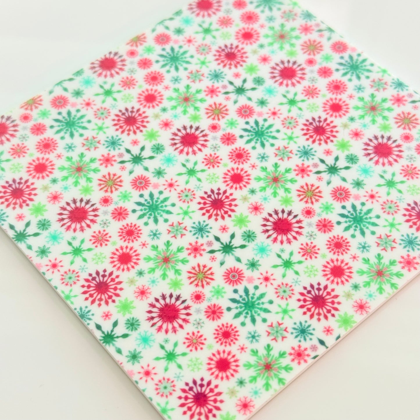 a square-shaped pattern with a repeating design of red and green snowflakes on a white background.