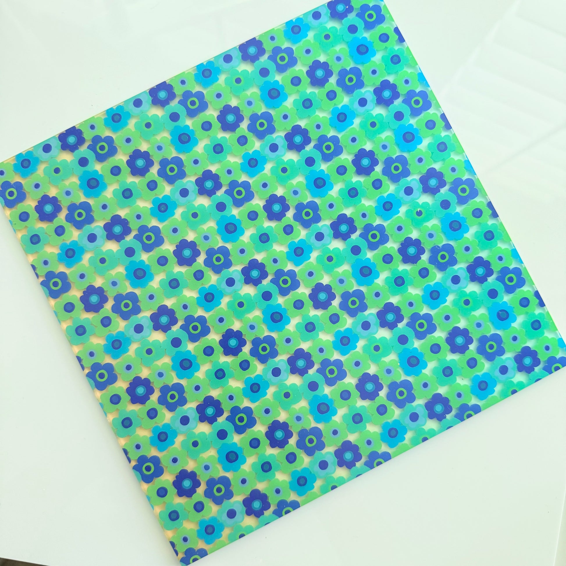 a square-shaped paper with a vibrant floral pattern in shades of blue and green.