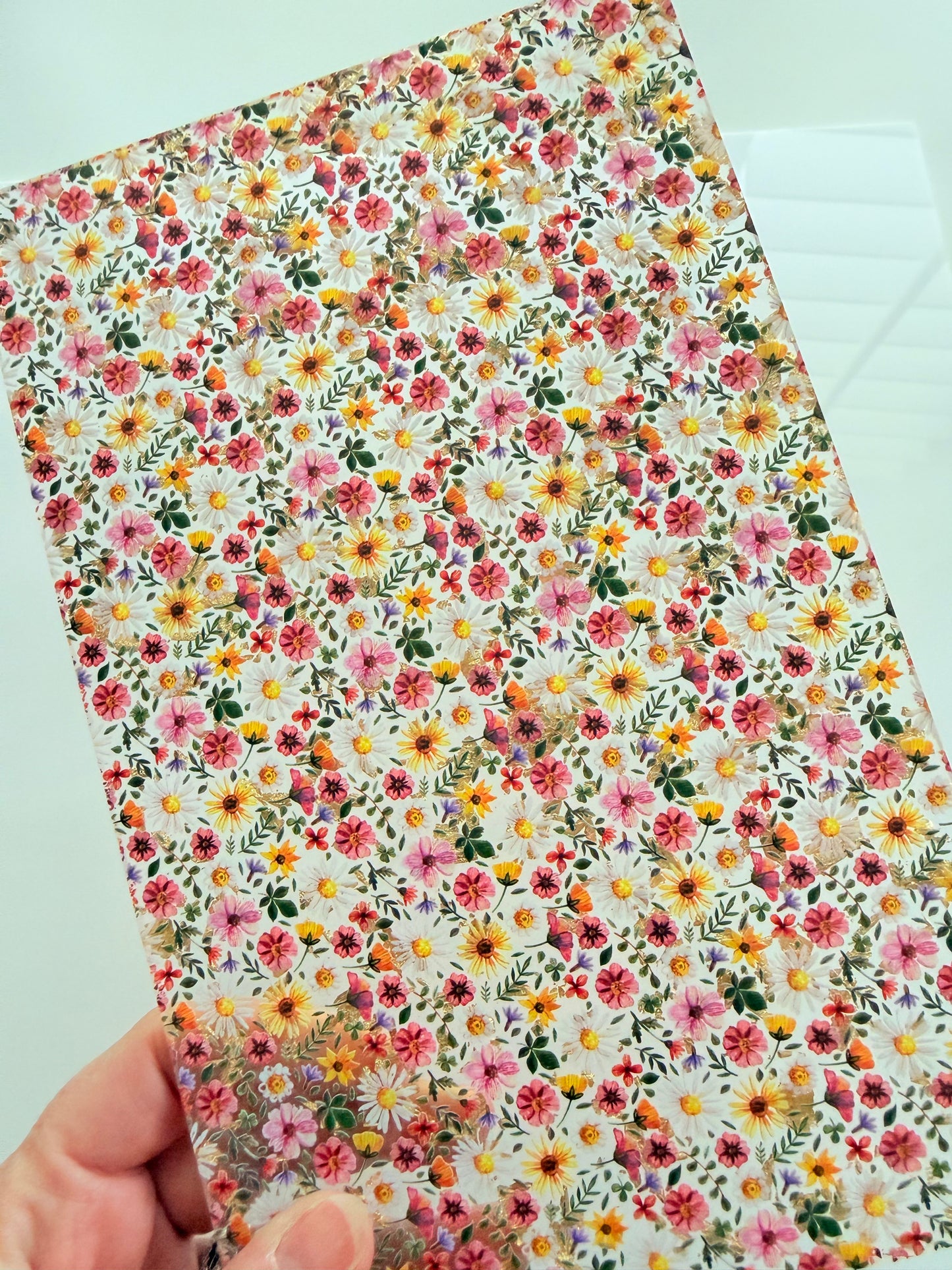 A hand is holding a piece of paper with a vibrant floral pattern on it.