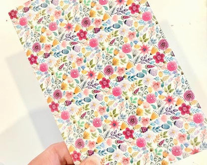 A hand is holding a colorful, patterned paper with a variety of flowers and leaves.